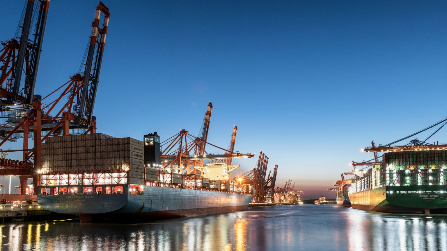 Container ships berthed under gantry cranes at a container terminal at dusk - ports recruitment by Sigma Search